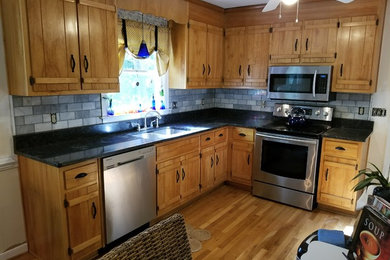 リッチモンドにある低価格の中くらいなトラディショナルスタイルのおしゃれなキッチン (ダブルシンク、中間色木目調キャビネット、御影石カウンター、青いキッチンパネル、磁器タイルのキッチンパネル、シルバーの調理設備、無垢フローリング、茶色い床) の写真