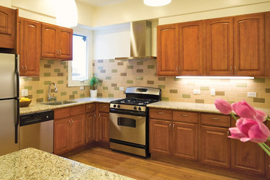 Example of a mid-sized classic l-shaped medium tone wood floor eat-in kitchen design in DC Metro with a double-bowl sink, raised-panel cabinets, medium tone wood cabinets, granite countertops, multicolored backsplash, ceramic backsplash, stainless steel appliances and an island