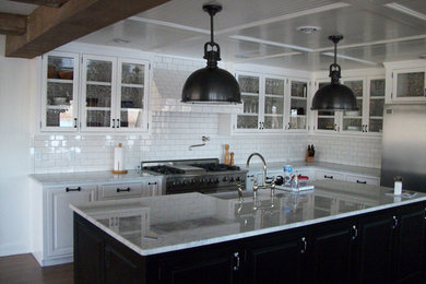 Example of a dark wood floor kitchen design in Other with a double-bowl sink, glass-front cabinets, white cabinets, granite countertops, white backsplash, subway tile backsplash, stainless steel appliances and an island