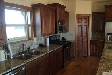 Example of a farmhouse l-shaped medium tone wood floor eat-in kitchen design in Wichita with a double-bowl sink, raised-panel cabinets, dark wood cabinets, granite countertops, stone tile backsplash, stainless steel appliances and an island