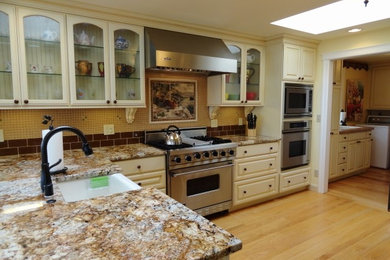 Example of a mid-sized classic l-shaped light wood floor eat-in kitchen design in Seattle with a farmhouse sink, raised-panel cabinets, white cabinets, granite countertops, yellow backsplash, glass tile backsplash, stainless steel appliances and a peninsula
