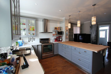Example of a mid-sized transitional u-shaped medium tone wood floor eat-in kitchen design in Toronto with a farmhouse sink, raised-panel cabinets, blue cabinets, wood countertops, white backsplash, stainless steel appliances, an island and subway tile backsplash