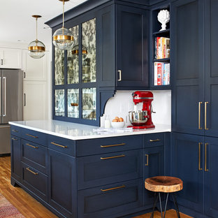 Diseño de cocina comedor clásica renovada, de tamaño medio, con fregadero de un seno, puertas de armario azules, encimera de cuarzo compacto, salpicadero blanco, salpicadero de azulejos tipo metro, electrodomésticos de acero inoxidable, suelo de madera en tonos medios, península, suelo marrón, encimeras blancas y armarios estilo shaker