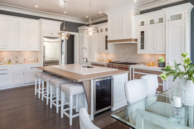 Example of a large transitional l-shaped dark wood floor eat-in kitchen design in New York with white cabinets, quartz countertops, beige backsplash, stainless steel appliances and an island