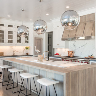 Immagine di una grande cucina costiera con paraspruzzi bianco, elettrodomestici in acciaio inossidabile, parquet chiaro, isola, ante bianche e ante con riquadro incassato