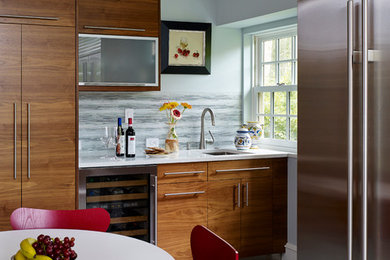 Cette image montre une cuisine américaine design en bois brun avec un évier encastré, un placard à porte plane, une crédence grise, un électroménager en acier inoxydable, un plan de travail en quartz modifié et une crédence en feuille de verre.