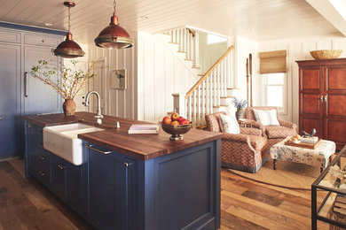 Example of a mid-sized country l-shaped medium tone wood floor open concept kitchen design in Orange County with an island, a farmhouse sink, recessed-panel cabinets, blue cabinets, wood countertops, white backsplash, ceramic backsplash and paneled appliances