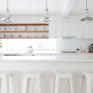 Inspiration for a mid-sized beach style single-wall kitchen in Sydney with an undermount sink, shaker cabinets, white cabinets, quartz benchtops, white splashback, subway tile splashback, stainless steel appliances, laminate floors, with island, beige floor and white benchtop.