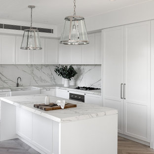 Photo of a mid-sized transitional l-shaped kitchen in Sydney with a farmhouse sink, shaker cabinets, white cabinets, white splashback, medium hardwood floors, with island, beige floor and white benchtop.