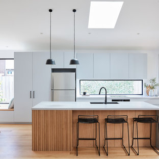 Photo of a mid-sized contemporary galley open plan kitchen in Melbourne with an undermount sink, grey cabinets, concrete benchtops, window splashback, light hardwood floors, with island, grey benchtop, flat-panel cabinets, stainless steel appliances and beige floor.