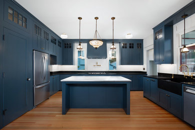 Inspiration for a large transitional u-shaped medium tone wood floor and brown floor kitchen remodel in Seattle with a farmhouse sink, shaker cabinets, blue cabinets, soapstone countertops, white backsplash, mosaic tile backsplash, stainless steel appliances, an island and black countertops