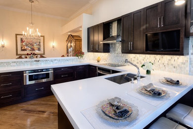 Transitional medium tone wood floor eat-in kitchen photo in Miami with an undermount sink, shaker cabinets, dark wood cabinets, quartzite countertops, white backsplash, glass tile backsplash and stainless steel appliances