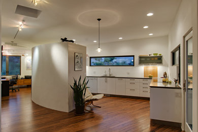 Example of a large trendy l-shaped dark wood floor and brown floor open concept kitchen design in Phoenix with an undermount sink, flat-panel cabinets, white cabinets, quartz countertops, white appliances and a peninsula