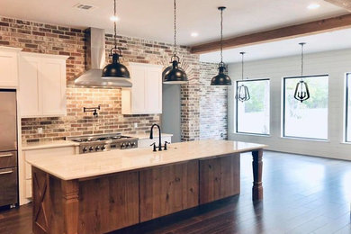 Example of a mid-sized country l-shaped medium tone wood floor and brown floor open concept kitchen design in Austin with a farmhouse sink, shaker cabinets, white cabinets, quartz countertops, brown backsplash, brick backsplash, stainless steel appliances, an island and white countertops