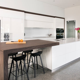This is an example of a contemporary galley kitchen in Perth with a double-bowl sink, flat-panel cabinets, white cabinets, white splashback, panelled appliances, with island, grey floor and white benchtop.