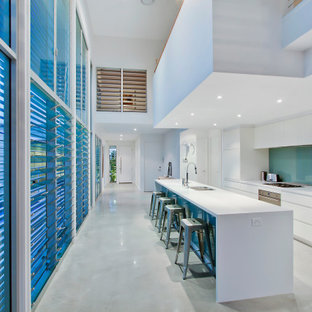 Design ideas for a contemporary galley kitchen in Gold Coast - Tweed with an undermount sink, flat-panel cabinets, white cabinets, blue splashback, glass sheet splashback, stainless steel appliances, with island, grey floor and white benchtop.
