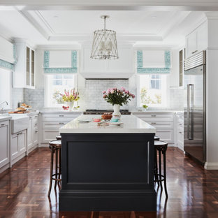 This is an example of a transitional u-shaped separate kitchen in Newcastle - Maitland with a farmhouse sink, recessed-panel cabinets, white cabinets, white splashback, marble splashback, stainless steel appliances, medium hardwood floors, with island, brown floor and multi-coloured benchtop.
