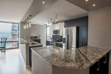 Modern inredning av ett litet kök, med en undermonterad diskho, släta luckor, svarta skåp, granitbänkskiva, svart stänkskydd, stänkskydd i glaskakel, rostfria vitvaror, ljust trägolv och en halv köksö
