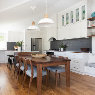 Photo of a traditional eat-in kitchen in Brisbane with a farmhouse sink, shaker cabinets, white cabinets, black splashback, medium hardwood floors and white benchtop.