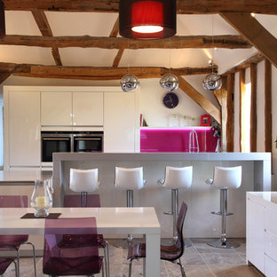 Aménagement d'une cuisine américaine parallèle contemporaine de taille moyenne avec un placard à porte plane, des portes de placard blanches, une crédence rose et une crédence en feuille de verre.