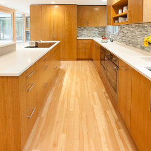 This is an example of a mid-sized midcentury u-shaped kitchen in Milwaukee with an undermount sink, flat-panel cabinets, medium wood cabinets, quartz benchtops, black splashback, glass tile splashback, stainless steel appliances, vinyl floors and with island.