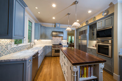 Large cottage u-shaped medium tone wood floor and brown floor enclosed kitchen photo in San Francisco with a farmhouse sink, beaded inset cabinets, blue cabinets, wood countertops, multicolored backsplash, mosaic tile backsplash, stainless steel appliances and an island