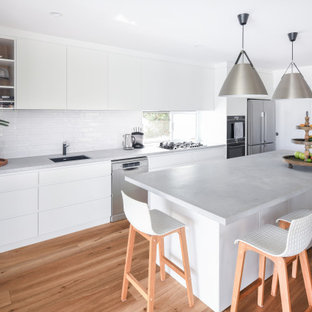 Photo of a mid-sized contemporary single-wall open plan kitchen in Sydney with an undermount sink, flat-panel cabinets, white cabinets, quartz benchtops, white splashback, ceramic splashback, stainless steel appliances, medium hardwood floors, with island, brown floor and grey benchtop.