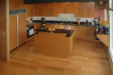 Example of a mid-sized minimalist l-shaped medium tone wood floor open concept kitchen design in Seattle with an undermount sink, flat-panel cabinets, medium tone wood cabinets, quartz countertops, black backsplash, paneled appliances and an island