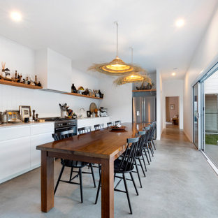 Design ideas for a large beach style single-wall eat-in kitchen in Sunshine Coast with flat-panel cabinets, white cabinets, stainless steel appliances, concrete floors, grey floor, an undermount sink, white splashback, timber splashback and white benchtop.