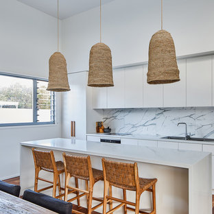 Photo of a beach style galley open plan kitchen in Gold Coast - Tweed with a drop-in sink, flat-panel cabinets, white cabinets, grey splashback, stainless steel appliances, dark hardwood floors, with island, brown floor and grey benchtop.
