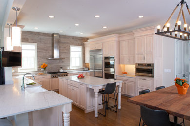 This is an example of a large traditional u-shaped open plan kitchen in Chicago with a belfast sink, raised-panel cabinets, light wood cabinets, quartz worktops, brown splashback, porcelain splashback, stainless steel appliances, medium hardwood flooring, an island, brown floors and grey worktops.