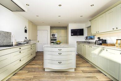 This is an example of a large traditional galley kitchen/diner in Hampshire with a submerged sink, shaker cabinets, green cabinets, granite worktops, beige splashback, stainless steel appliances, porcelain flooring, an island, beige floors and beige worktops.