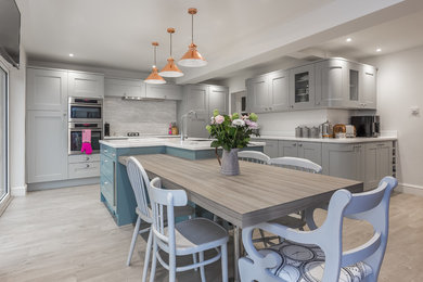 Photo of a medium sized bohemian l-shaped kitchen/diner in Hampshire with laminate floors, beige floors, a submerged sink, shaker cabinets, grey cabinets, composite countertops, grey splashback, stainless steel appliances, an island and white worktops.