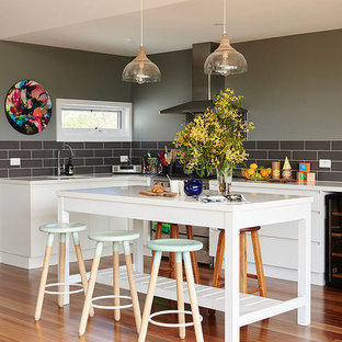 Large transitional l-shaped open plan kitchen in Melbourne with an undermount sink, white cabinets, quartz benchtops, ceramic splashback, stainless steel appliances, with island, orange floor, flat-panel cabinets, black splashback and medium hardwood floors.