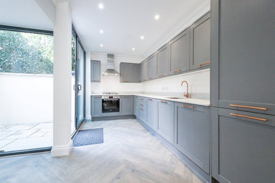 Inspiration for a medium sized victorian l-shaped kitchen/diner in London with a built-in sink, flat-panel cabinets, grey cabinets, granite worktops, white splashback, coloured appliances, light hardwood flooring, no island, grey floors and white worktops.