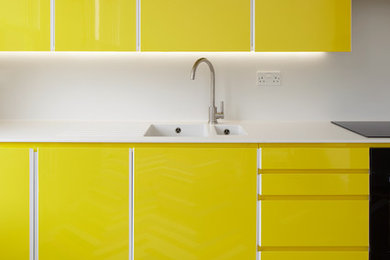 На фото: кухня в современном стиле с двойной мойкой, плоскими фасадами, желтыми фасадами, белым фартуком, деревянным полом и разноцветным полом с