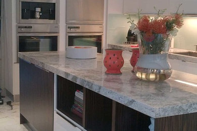 Example of a large trendy l-shaped marble floor and white floor eat-in kitchen design in Miami with flat-panel cabinets, white cabinets, marble countertops, glass sheet backsplash, an island, stainless steel appliances, an undermount sink and blue backsplash