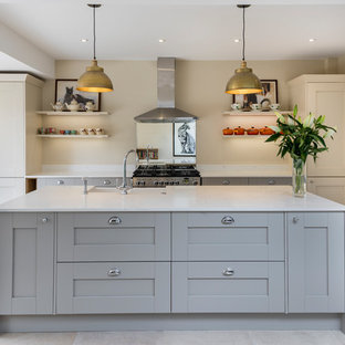 Photo of a medium sized classic galley kitchen in London with shaker cabinets, stainless steel appliances, an island, white worktops, a belfast sink, grey cabinets and beige floors.