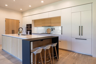 Inspiration for a huge modern single-wall light wood floor and brown floor eat-in kitchen remodel in Portland with an undermount sink, flat-panel cabinets, light wood cabinets, quartz countertops, white backsplash, glass sheet backsplash, paneled appliances, an island and white countertops