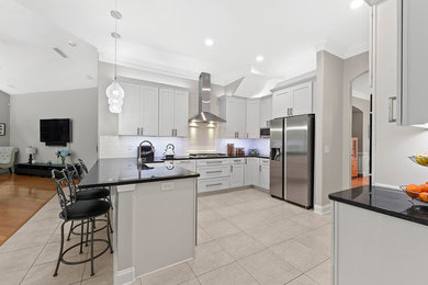 Example of a mid-sized minimalist l-shaped ceramic tile and beige floor eat-in kitchen design in Jacksonville with a farmhouse sink, shaker cabinets, white cabinets, granite countertops, white backsplash, subway tile backsplash, stainless steel appliances, a peninsula and black countertops