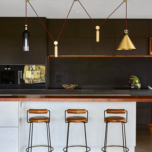 This is an example of a large contemporary galley kitchen in Brisbane with flat-panel cabinets, dark wood cabinets, black splashback, black appliances, with island, black benchtop and grey floor.