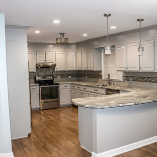 Mid-sized traditional eat-in kitchen ideas - Inspiration for a mid-sized timeless l-shaped medium tone wood floor and brown floor eat-in kitchen remodel in Charleston with an undermount sink, raised-panel cabinets, gray cabinets, quartzite countertops, gray backsplash, glass sheet backsplash, stainless steel appliances, a peninsula and gray countertops