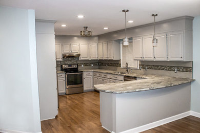 Inredning av ett klassiskt mellanstort grå grått kök, med en undermonterad diskho, luckor med upphöjd panel, grå skåp, bänkskiva i kvartsit, grått stänkskydd, glaspanel som stänkskydd, rostfria vitvaror, mellanmörkt trägolv, en halv köksö och brunt golv