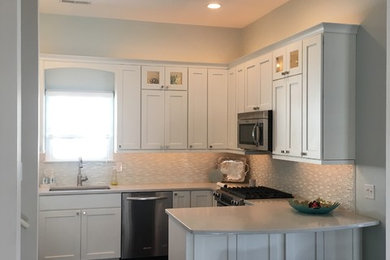 Inredning av ett modernt kök, med en undermonterad diskho, skåp i shakerstil, vita skåp, bänkskiva i kvarts, flerfärgad stänkskydd, stänkskydd i glaskakel, rostfria vitvaror, mörkt trägolv, en halv köksö och brunt golv