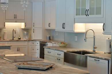 Example of a mid-sized beach style l-shaped medium tone wood floor and brown floor open concept kitchen design in DC Metro with a farmhouse sink, shaker cabinets, white cabinets, granite countertops, white backsplash, glass tile backsplash, stainless steel appliances, an island and beige countertops