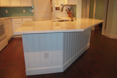 Example of a mid-sized beach style u-shaped porcelain tile kitchen pantry design in Orlando with a double-bowl sink, shaker cabinets, white cabinets, quartz countertops, blue backsplash, glass tile backsplash, white appliances and a peninsula