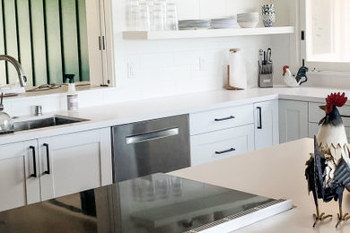 Maritim inredning av ett vit vitt kök och matrum, med en undermonterad diskho, skåp i shakerstil, vita skåp, bänkskiva i kvarts, vitt stänkskydd, stänkskydd i tunnelbanekakel, rostfria vitvaror och en köksö