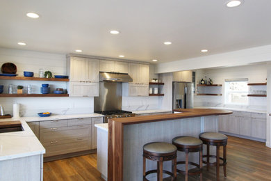 Mid-sized beach style l-shaped vinyl floor and brown floor open concept kitchen photo in Other with an undermount sink, shaker cabinets, light wood cabinets, quartz countertops, white backsplash, quartz backsplash, stainless steel appliances, an island and white countertops