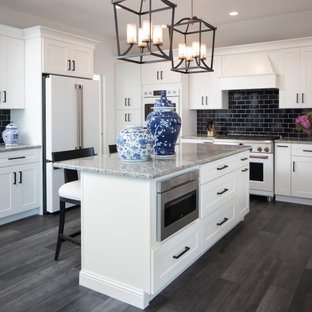 Photo of a transitional u-shaped kitchen in New York with shaker cabinets, white cabinets, black splashback, subway tile splashback, white appliances, medium hardwood floors, with island, brown floor and multi-coloured benchtop.