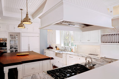Inspiration for a timeless l-shaped medium tone wood floor enclosed kitchen remodel in Boston with a farmhouse sink, shaker cabinets, white cabinets, marble countertops, white backsplash, subway tile backsplash, stainless steel appliances and an island